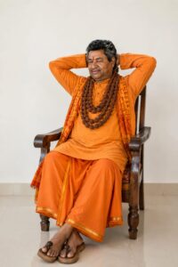तथाकथित फर्जी पुजारी सुरेश तिवारी,संत वेश-भूषा में खड़ाऊं पहनकर मन्दिर की जमीन पर अपना घर बनवाते हुए